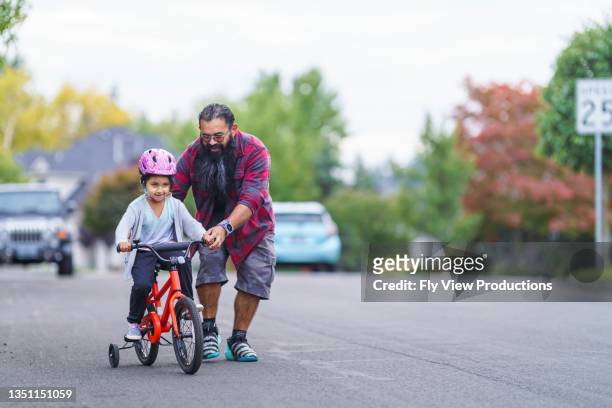 native american dad helping his young daughter learn to ride a bike - training wheels stock pictures, royalty-free photos & images
