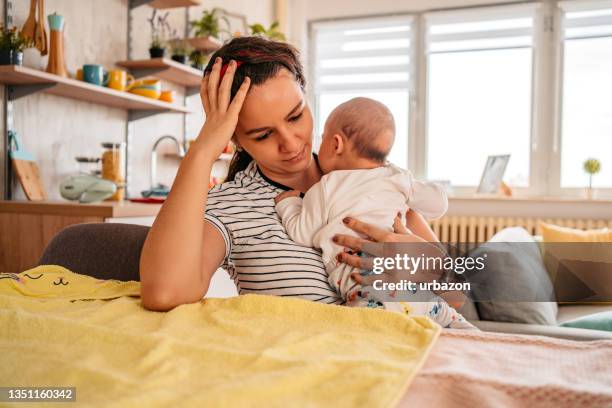 mother holding her newborn baby feeling sleepy - mothers babies stockfoto's en -beelden