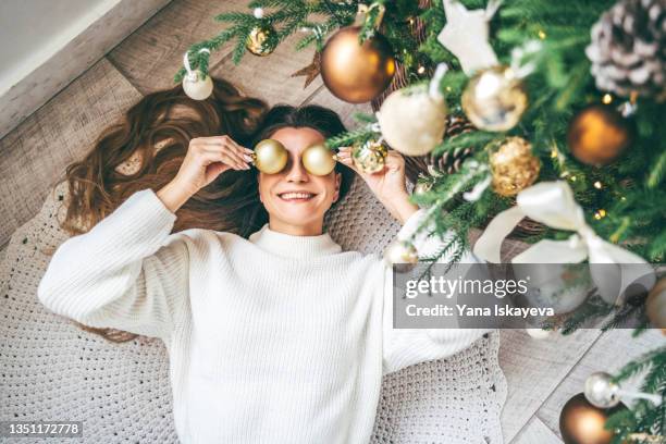 woman having fun with christmas balls lying under the decorated fir tree - decorare l'albero di natale foto e immagini stock
