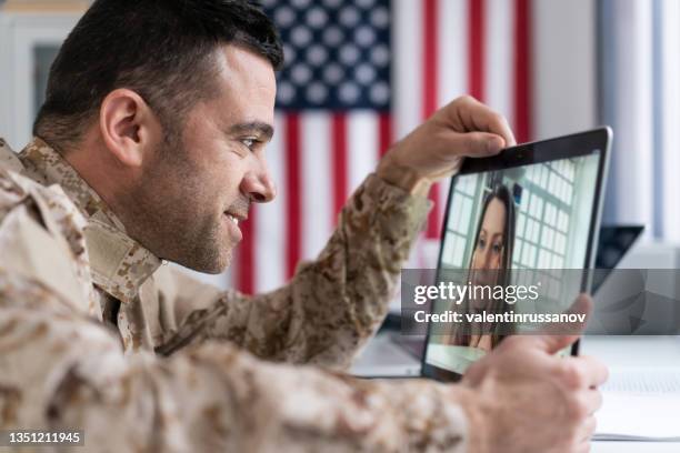 mid adult military soldier making teleconferencing with his wife on laptop in the office with american flag on the wall. - working wife stock pictures, royalty-free photos & images