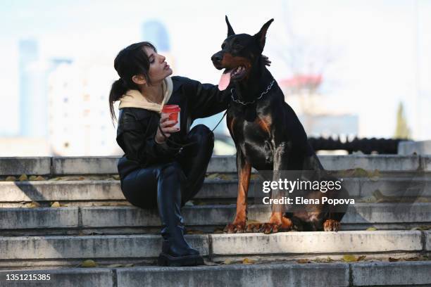 young woman wearing black leather clothes walking with doberman pinscher at the city street - white doberman pinscher stock pictures, royalty-free photos & images