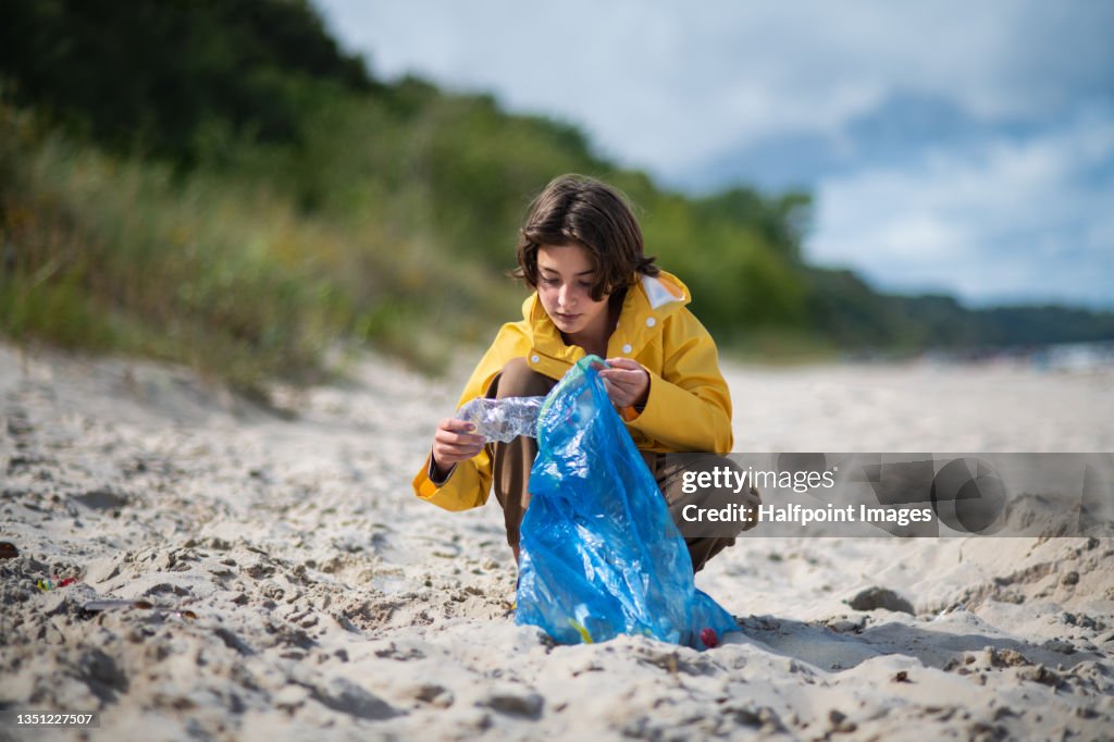Preteen ecological girl cleaning beach from plastic waste.