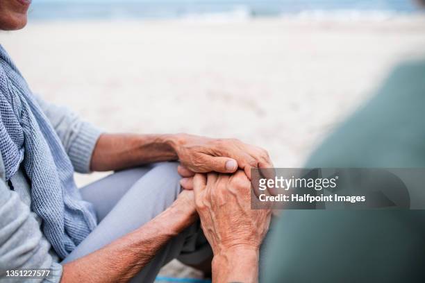 close up of senior couple in love sitting and holding hands on beach. - hands behind back bildbanksfoton och bilder