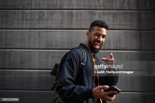 portrait of man commuter with smartphone doing grimace looking at camera outdoors in street. - winking fotografías e imágenes de stock