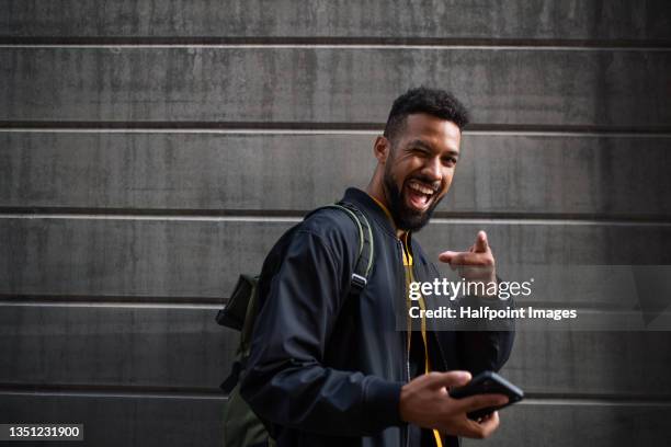 portrait of man commuter with smartphone doing grimace looking at camera outdoors in street. - taquiner photos et images de collection