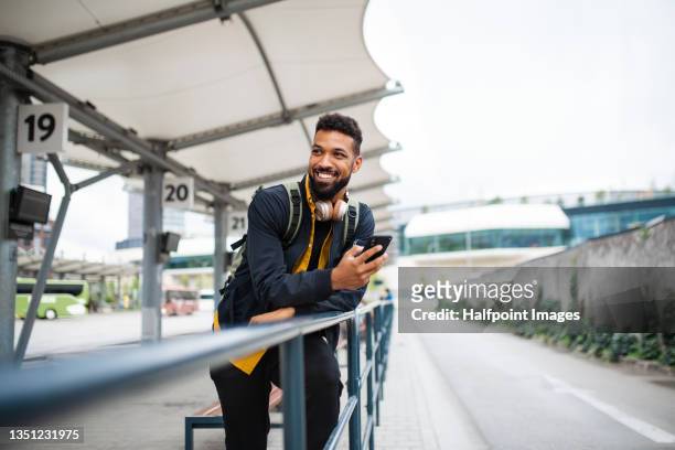 portrait of man commuter at the bus station using smartphone and waiting for bus. - city life stock pictures, royalty-free photos & images