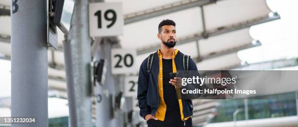 low angle view of man commuter at the bus station using smartphone and waiting for bus. - mann bus smartphone stock-fotos und bilder