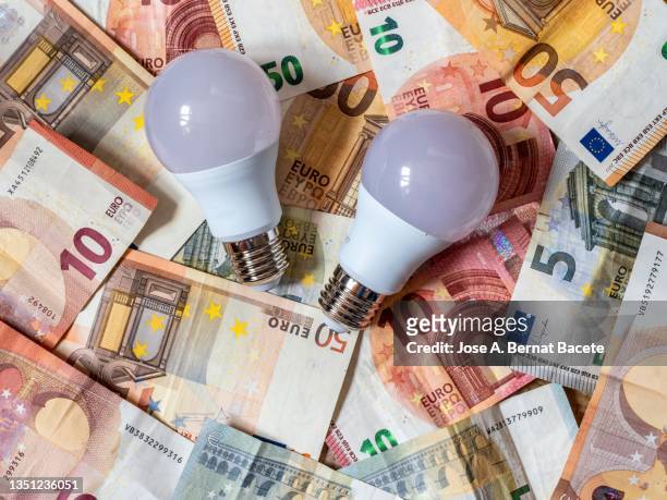 low consumption led light bulb and euro banknotes and coins - energie industrie stockfoto's en -beelden