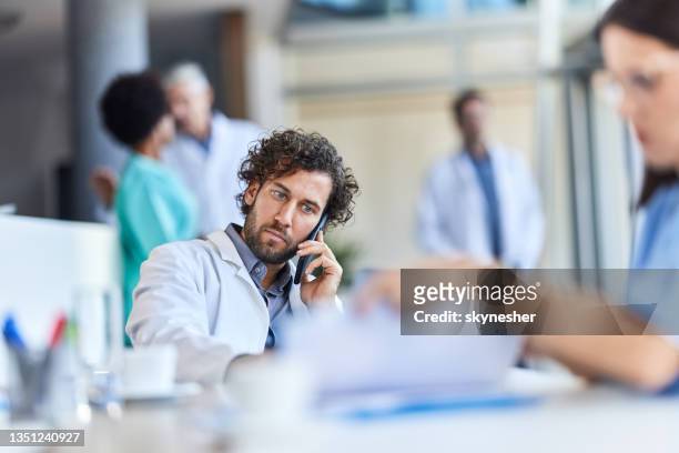 young doctor talking on cell phone while working on laptop in his office. - paramedics stock pictures, royalty-free photos & images