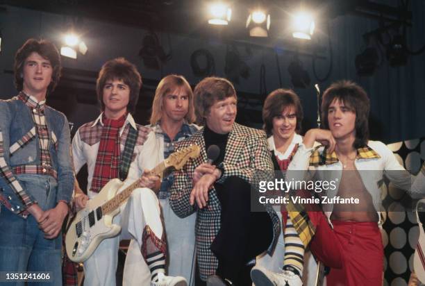British pop group the Bay City Rollers with a man wearing a tweed sports jacket holding a microphone, circa 1975. Possibly a television appearance by...