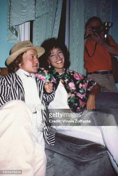British actor David Rappaport , wearing a black-and-white striped blazer and a Panama hat, and American actress Jennifer Beals, wearing a white...