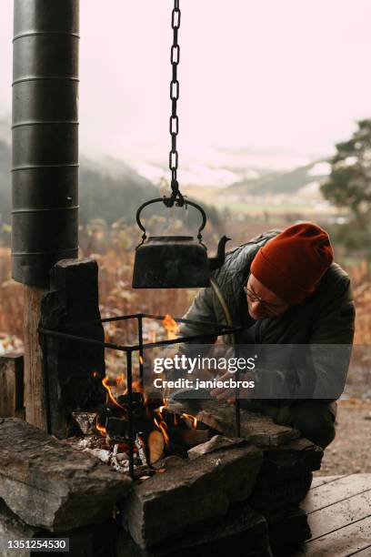 hombre vigilando el hogar. cabaña de madera con porche rodeada de montañas. viaje de otoño - mountian fire fotografías e imágenes de stock