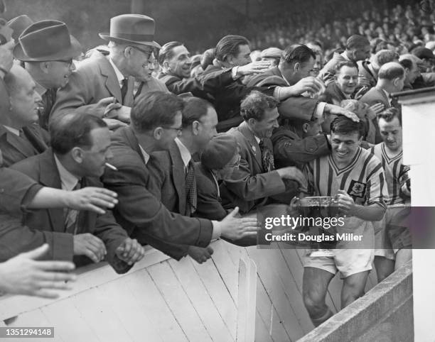Aston Villa Football Club team captain Johnny Dixon is congratulated by supporting team fans as he walks down the steps holding the Football...