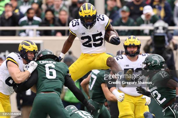 Hassan Haskins of the Michigan Wolverines jumps over Angelo Grose of the Michigan State Spartans during a first half run at Spartan Stadium on...