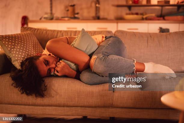 sad woman lying on sofa embracing pillow - woman curled up stock pictures, royalty-free photos & images