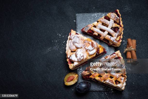 tre pezzi di torta americana con prugne su una tavola di pietra nera per servire su uno sfondo nero - crostata di frutta foto e immagini stock