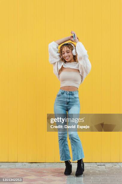 cheerful hispanic woman with smartphone listening to music - fashion pretty woman listening music in headphones with smartphone colorful photos et images de collection
