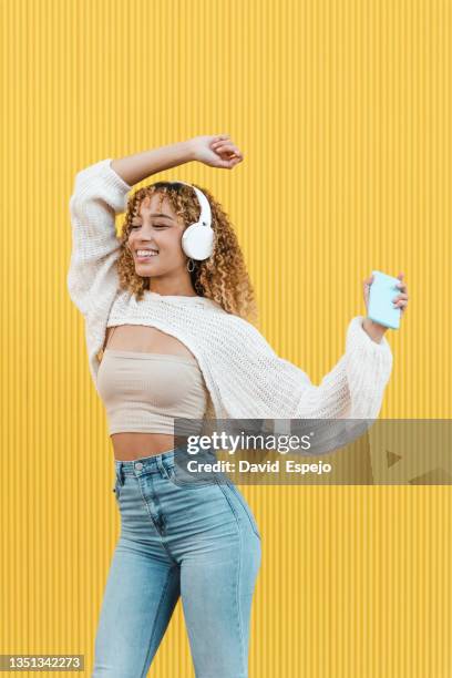 cheerful hispanic woman with smartphone listening to music - fashion pretty woman listening music in headphones with smartphone colorful photos et images de collection