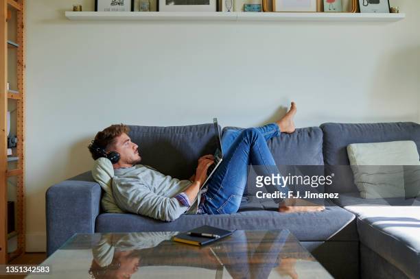 man using laptop in living room at home - jeans barefoot fotografías e imágenes de stock
