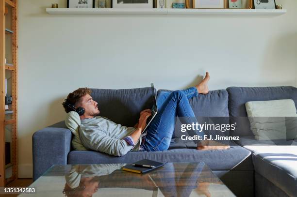 man using laptop in living room at home - barefoot stock photos et images de collection