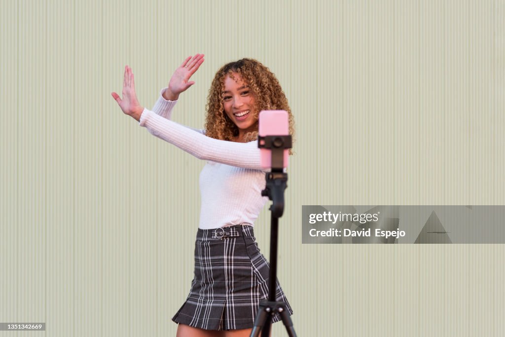 Cheerful Hispanic woman going live on smartphone