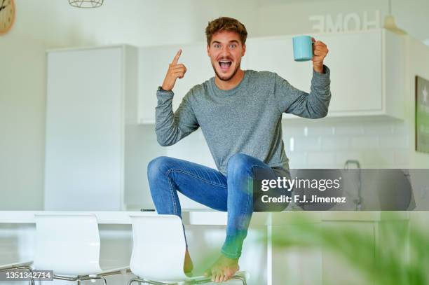 happy man with cup of coffee sitting in kitchen - küche überrascht mann stock-fotos und bilder