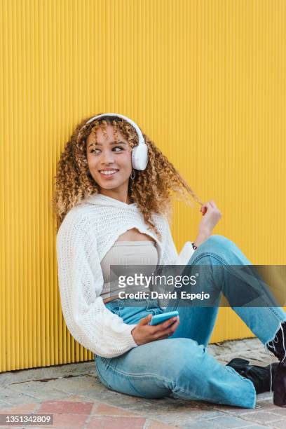 positive hispanic woman in headphones with smartphone - fashion pretty woman listening music in headphones with smartphone colorful stockfoto's en -beelden