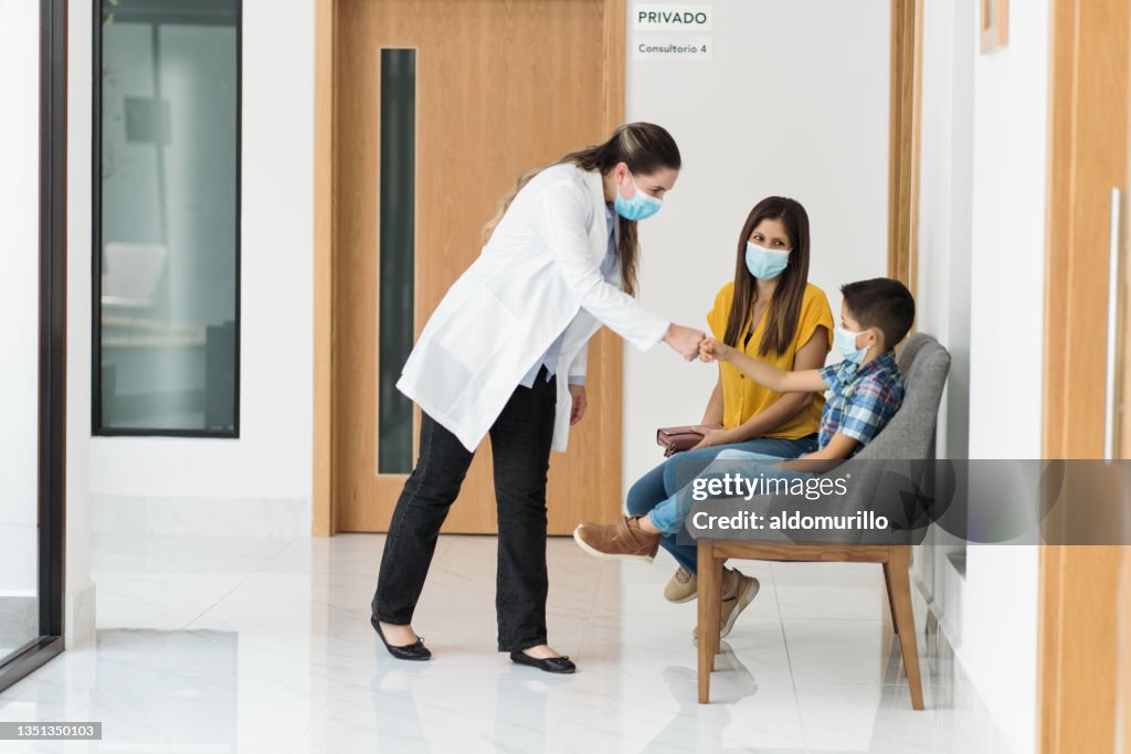 Female psychologist with mask shaking hands with boy in clinic
