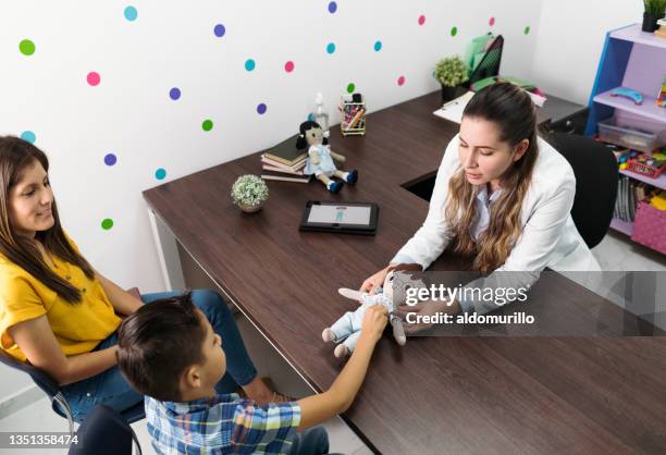 female psychologist holding boy doll and showing to boy in office - child psychologist stock pictures, royalty-free photos & images