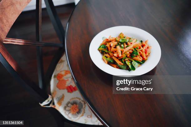 whole wheat penne pasta with marinara sauce and spinach in bowl on kitchen table - whole wheat penne pasta stock pictures, royalty-free photos & images