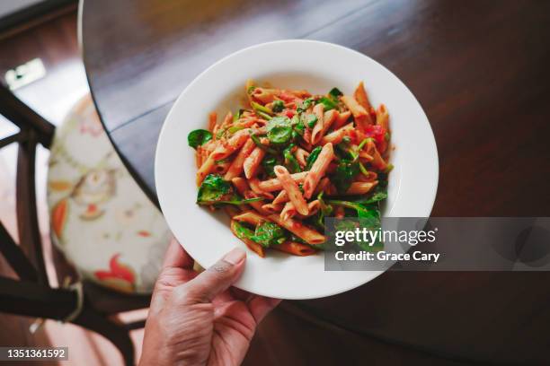 woman carries whole wheat penne pasta dish to kitchen table - whole wheat penne pasta stock pictures, royalty-free photos & images