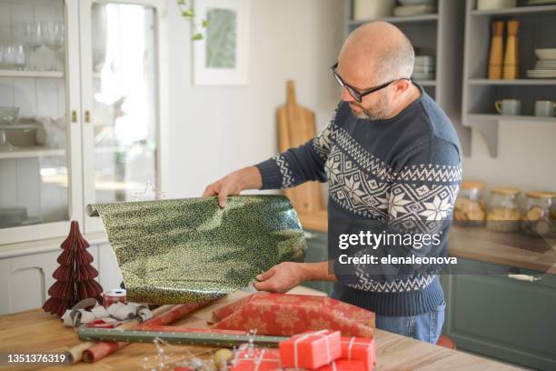 reifer erwachsener mann im weihnachtlichen zuhause (weihnachtsgeschenke einwickeln) - weihnachtspullover mann stock-fotos und bilder