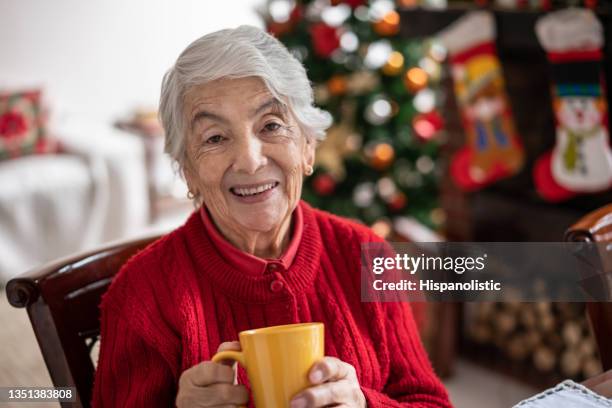 latin american beautiful senior woman at home enjoying a cup of hot chocolate on a joyful christmas day - traditional colombian clothing stock pictures, royalty-free photos & images