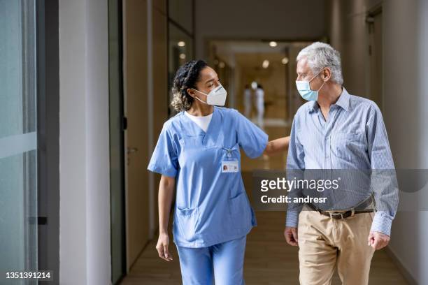 médico hablando con un paciente en el pasillo de un hospital mientras usa máscaras faciales - hospital fotografías e imágenes de stock