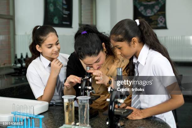 two girl students with teacher using microscope for laboratory experiment - school science lab stock pictures, royalty-free photos & images