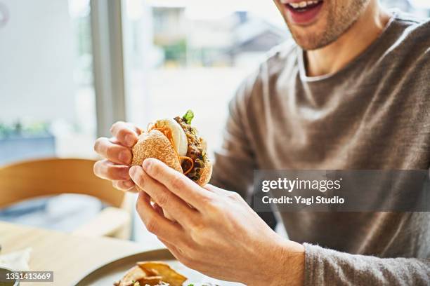 asian man eating a veggie burger at a vegan cafe. - vegetarian stock-fotos und bilder