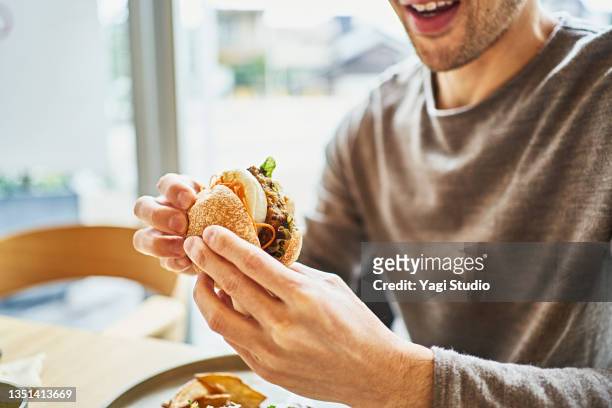 asian man eating a veggie burger at a vegan cafe. - 人体部位 ストックフォトと画像