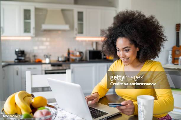 smiling young woman holding a credit card and typing on a laptop. - yellow shirt stock pictures, royalty-free photos & images