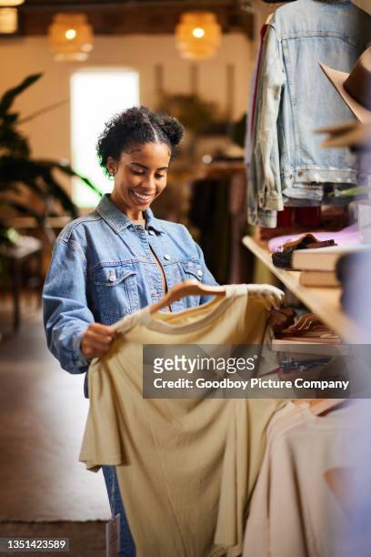 lächelnde frau, die beim einkaufen in einem bekleidungsgeschäft auf das hemd schaut - fashion store frau stock-fotos und bilder