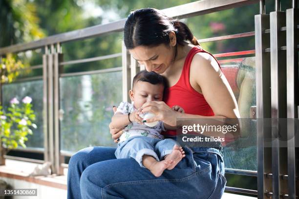 young mother feeding her son from milk bottle - mother son milk imagens e fotografias de stock