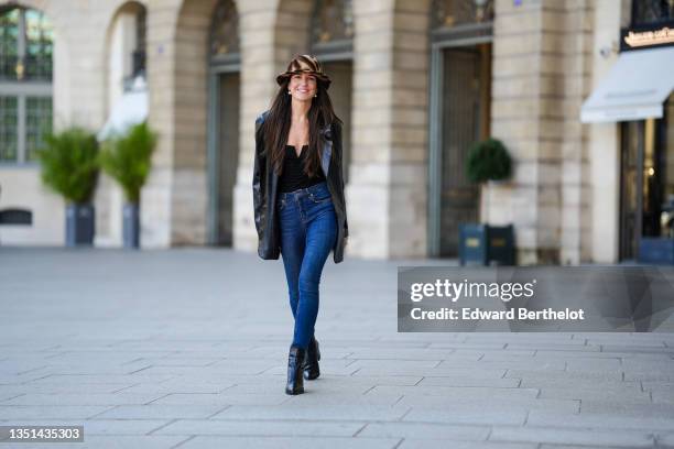 Alba Garavito Torre wears a brown and beige print pattern fluffy hat, gold pearls pendant earrings, a black V-neck / shoulder-off t-shirt, a black...