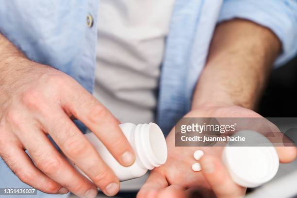 close-up view of man in blue button-down shirt placing a pill in his hand - aspirina foto e immagini stock
