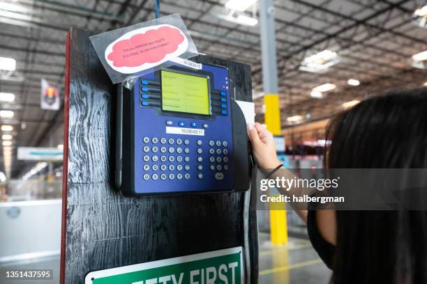 masked employee swiping a time card at fulfillment center - time clock stock pictures, royalty-free photos & images