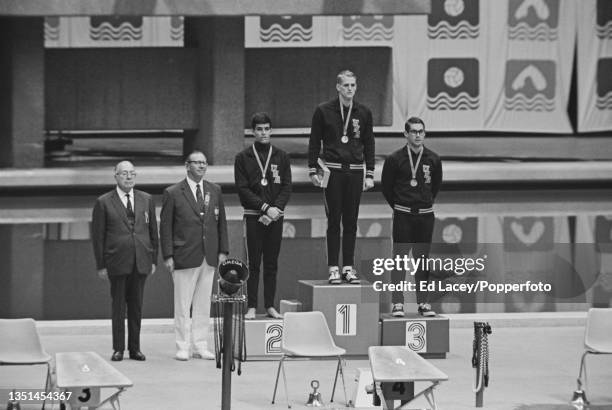 American swimmer Doug Russell of the United States team stands in centre on the podium after winning the gold medal in the Men's 100 metre butterfly...