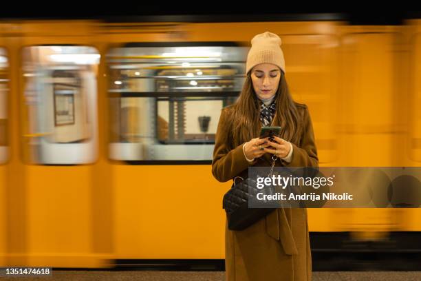 woman is looking on mobile while yellow subway passing behind her - budapest metro stock pictures, royalty-free photos & images