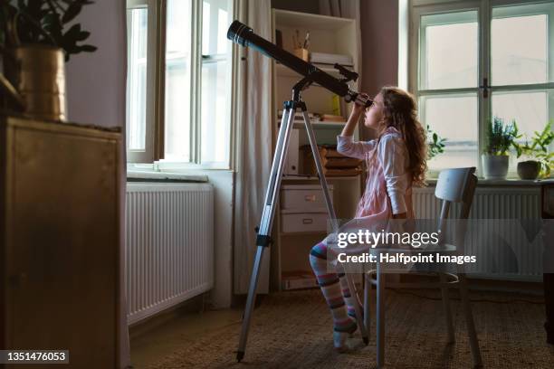 little girl looking through telescope indoors at home. - house science stock pictures, royalty-free photos & images