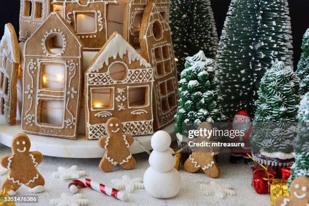 image cake stand of homemade, tiered christmas cake, cake covered with fondant icing and gingerbread house biscuits decorated with white royal icing, illuminated fairy lights, santa claus, gingerbread men, christmas tree cupcakes - christmas cake stock pictures, royalty-free photos & images