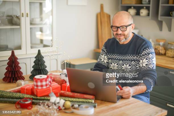 mature adult man in christmas home interior ( on-line shopping) - holiday shopping stock pictures, royalty-free photos & images
