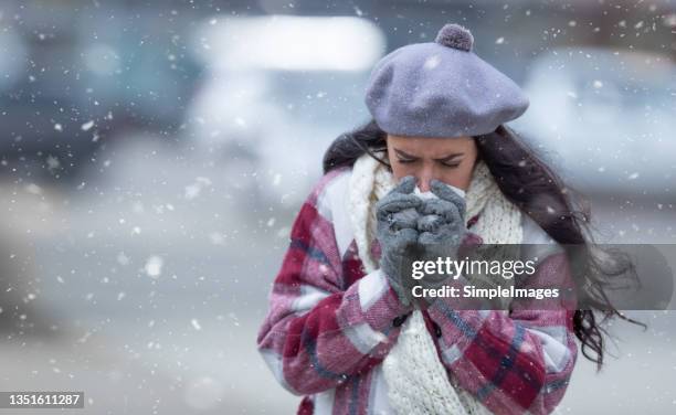 freezing winter day in the city with snow falling where fashionable woman cleans her nose into a napkin. - luft krank stock-fotos und bilder