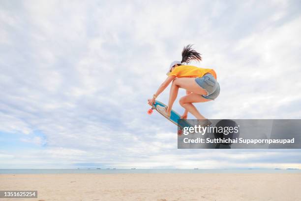 asian woman jumping with skateboard on the beach. - skateboard foto e immagini stock